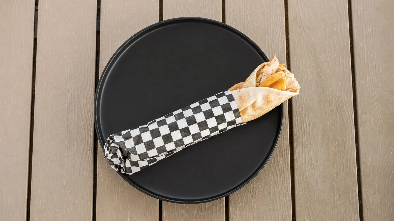 Grilled chicken shawarma wrap in checkered paper on a black plate