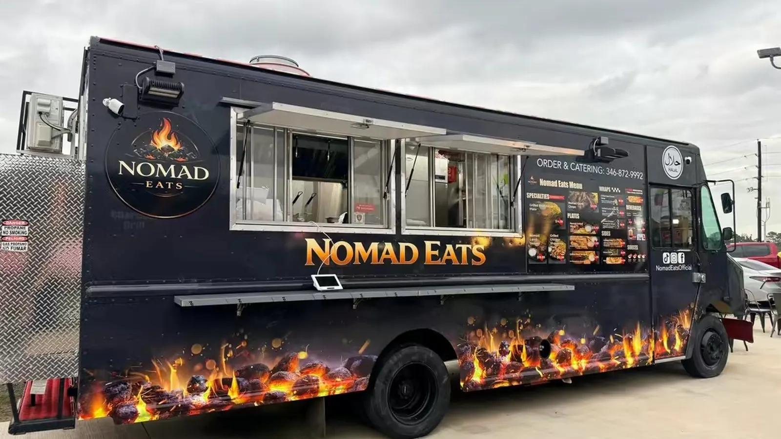 The Nomad Eats truck from the serving side — black with a flame graphic along the bottom, the window open